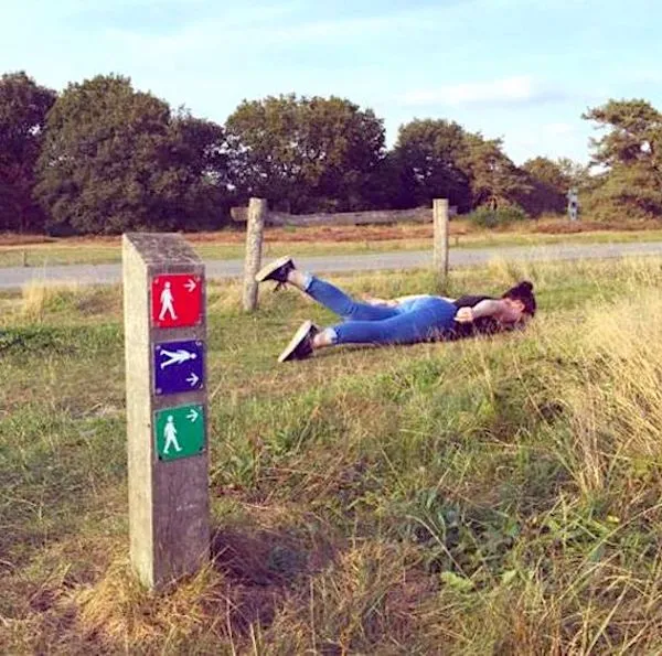 Osoba ležiaca pri turistických značkách na lúke, žartovná scénka v prírode.