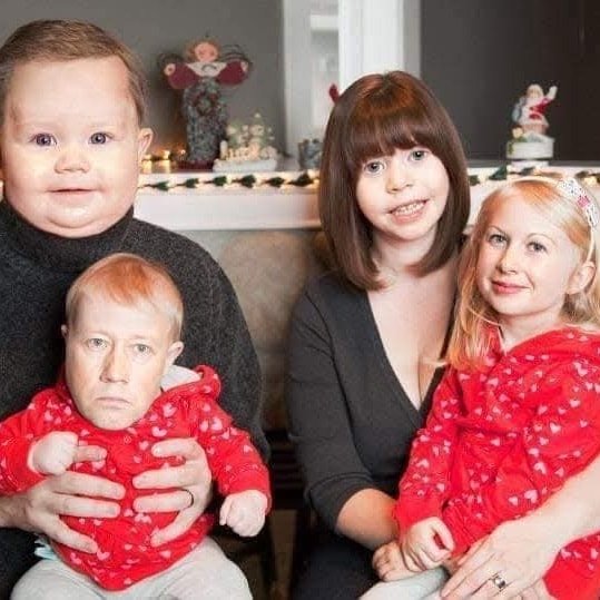 Rodina s vymenenými tvárami sedí spolu pred vianočnou výzdobou, úsmevy vyvolávajú humorný dojem.