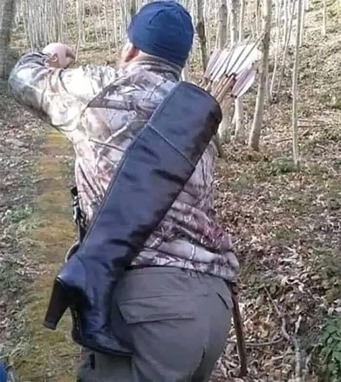 Osoba s tulecom plným šípov, oblečená v maskáčoch, kráča lesnou cestičkou v chladnom počasí.