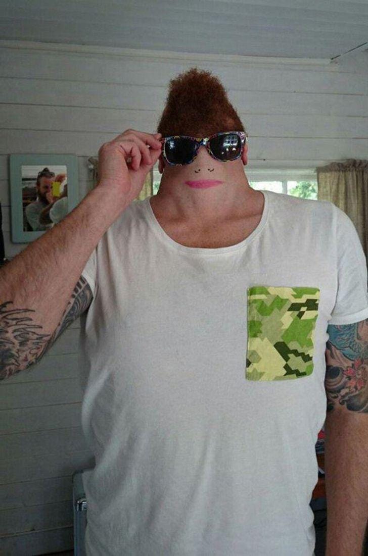 Muž s tetovaním a tričkom s vreckom na maskovanie humorne nosí okuliare na nesprávnom mieste na krku.
