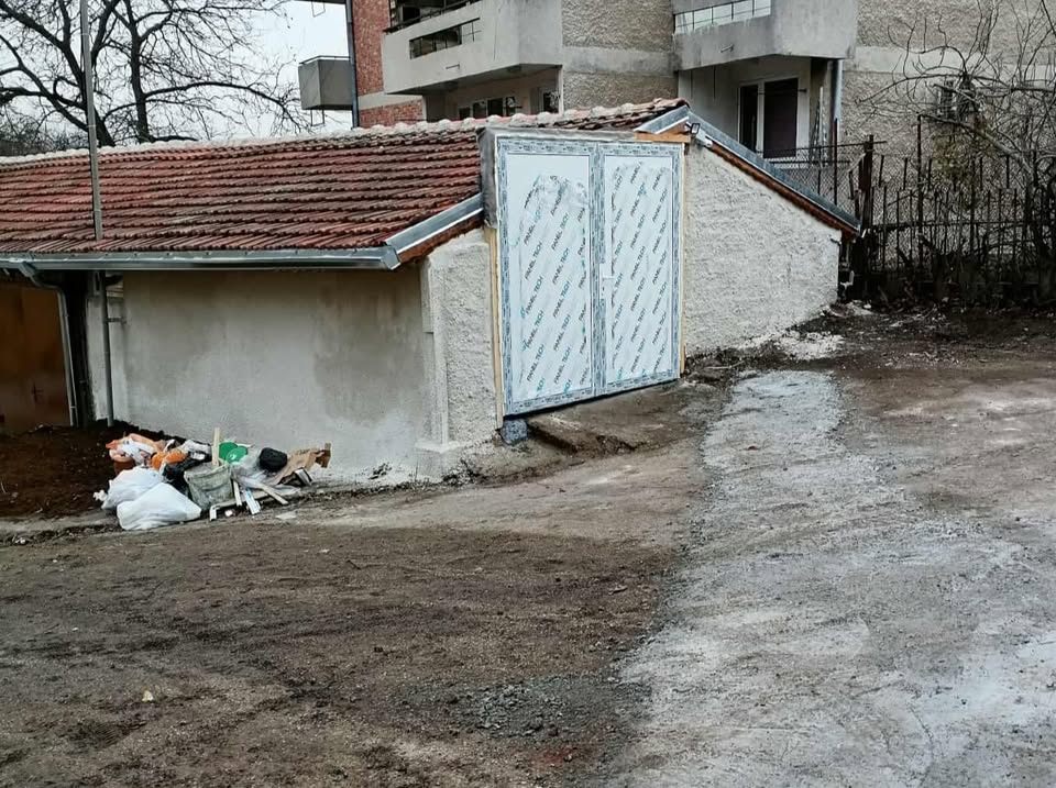 Stavenisko s novou dvojkrídlovou bránou na dome, vedľa neporiadok so stavebným materiálom.