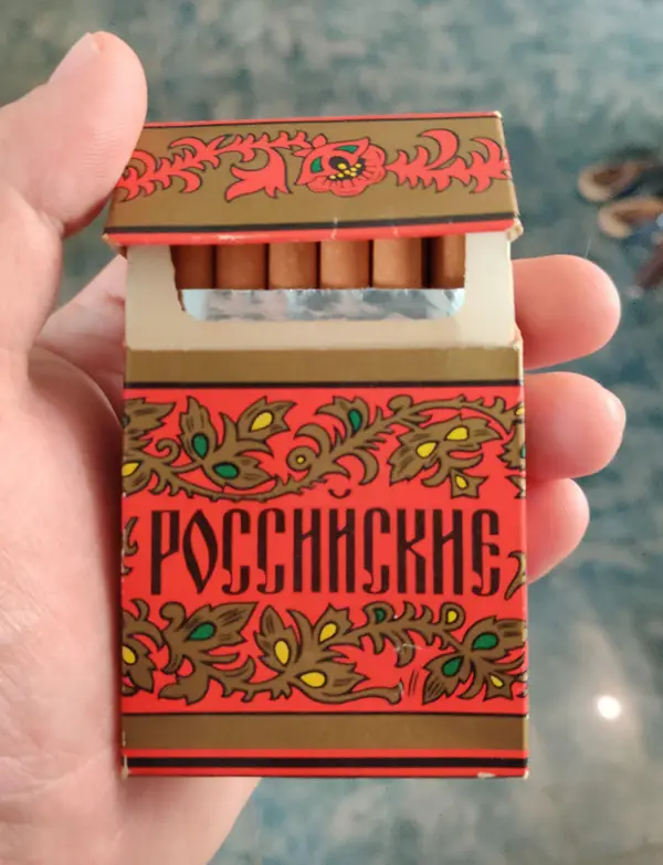 Krabička tradičných cigariet s ruským dizajnom v ruke na modrom pozadí.