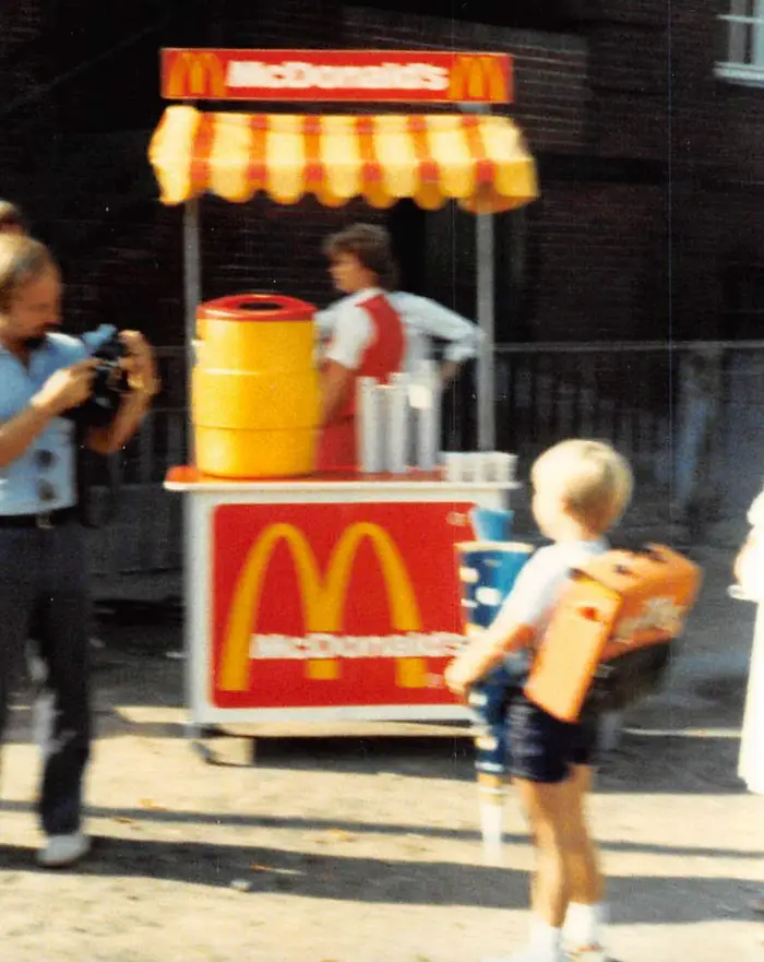 Dieťa pri stánku McDonald's na ulici, s fotoaparátom a barelom na limonádu, 80. roky.