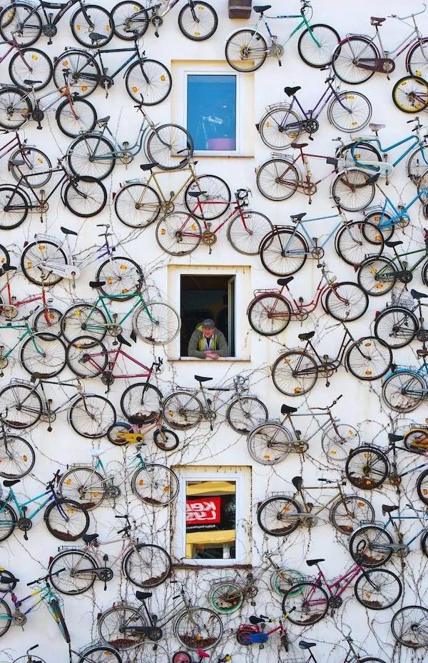 Muž pozerajúci z okna budovy pokrytej bicyklami, kreatívna dekorácia na stene, mestská umelecká inštalácia.