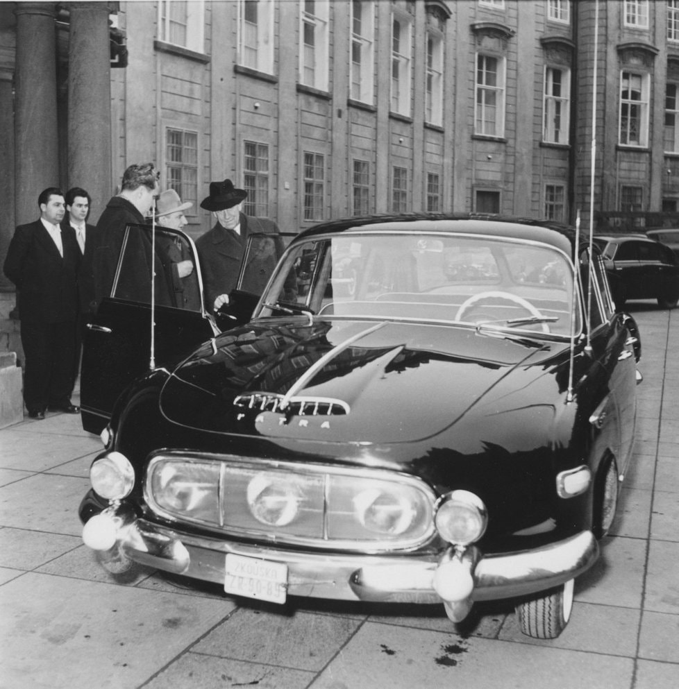 Vintage auto Tatra 603 stojí pred historickou budovou, okolo auta skupina ľudí v dobovom oblečení.