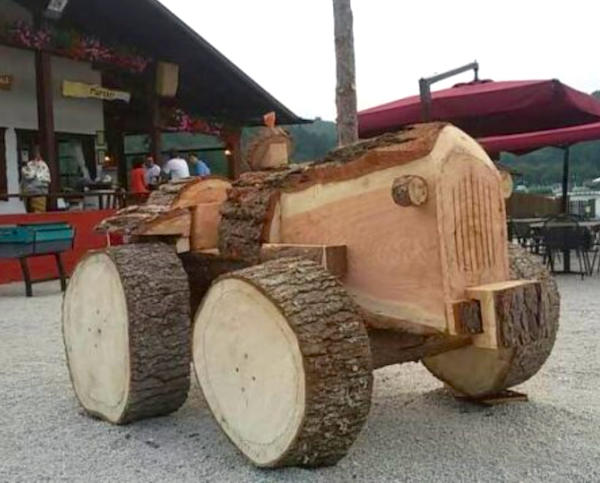 Drevený traktor zo stromových pňov pri reštaurácii s červeným slnečníkom v prírodnom prostredí.