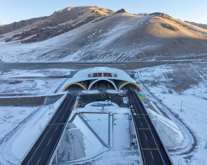 Horský tunel v zasneženej krajine s cestou, vedúci k zasneženým kopcom pod modrou oblohou.