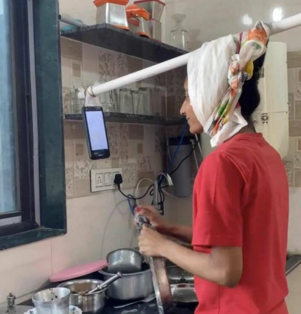 Osoba v kuchyni používa telefón zavesený na tyči na sledovanie videí počas varenia.