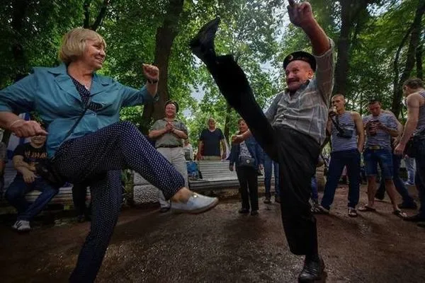 Dve osoby tancujú v parku, zatiaľ čo ich sleduje skupina ľudí.