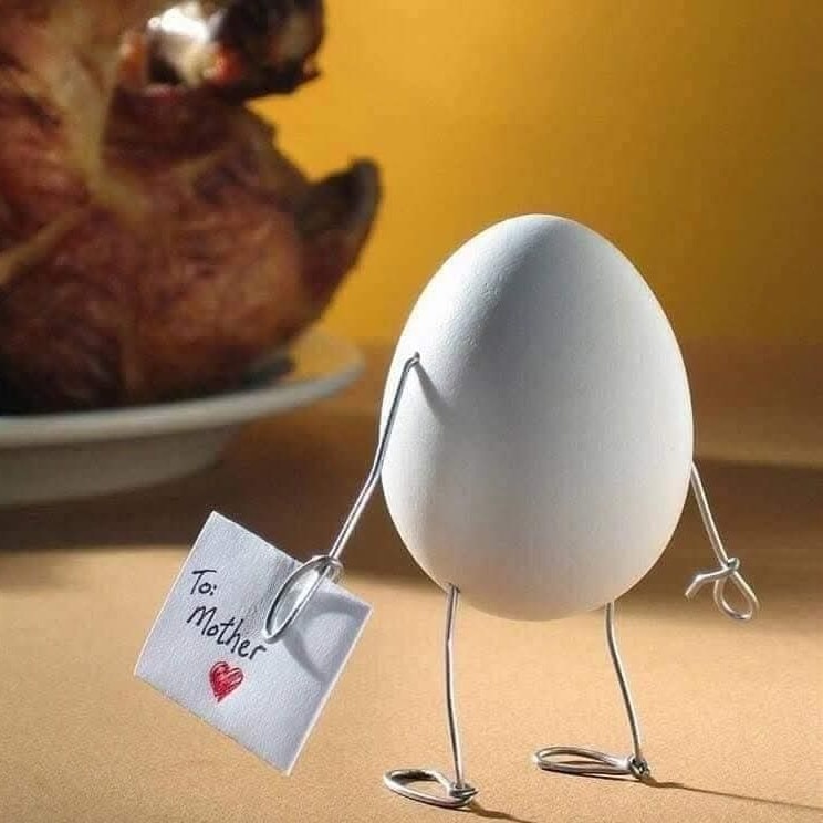 Vajce s nohami z drôtu drží lístok s nápisom To: Mother a stojí pred upečenou sliepkou na stole.