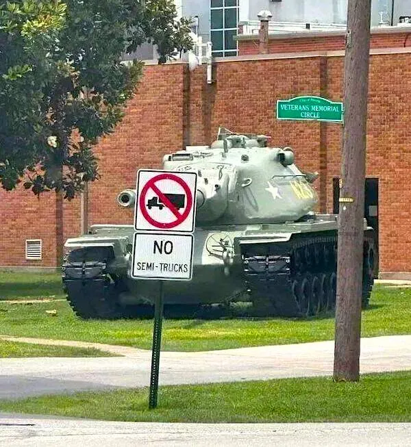 Tank zaparkovaný pri budove s dopravnou značkou zakazujúcou vjazd kamiónov.