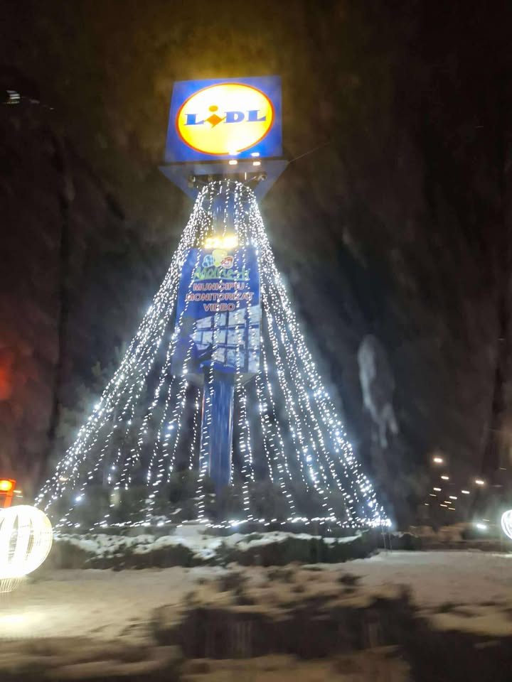 Osvetlený vianočný stromček v tvare loga Lidl, žiariace svetlá na zasneženej nočnej scéne.