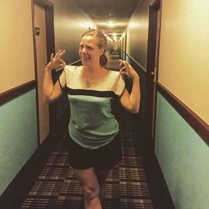 Žena stojí v hotelovej chodbe a robí žartovnú pózu, oblečená v pruhovanom tričku.