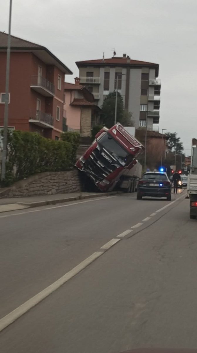 Kamión naklonený na obrubník pri dome, polícia na mieste, dopravná nehoda.
