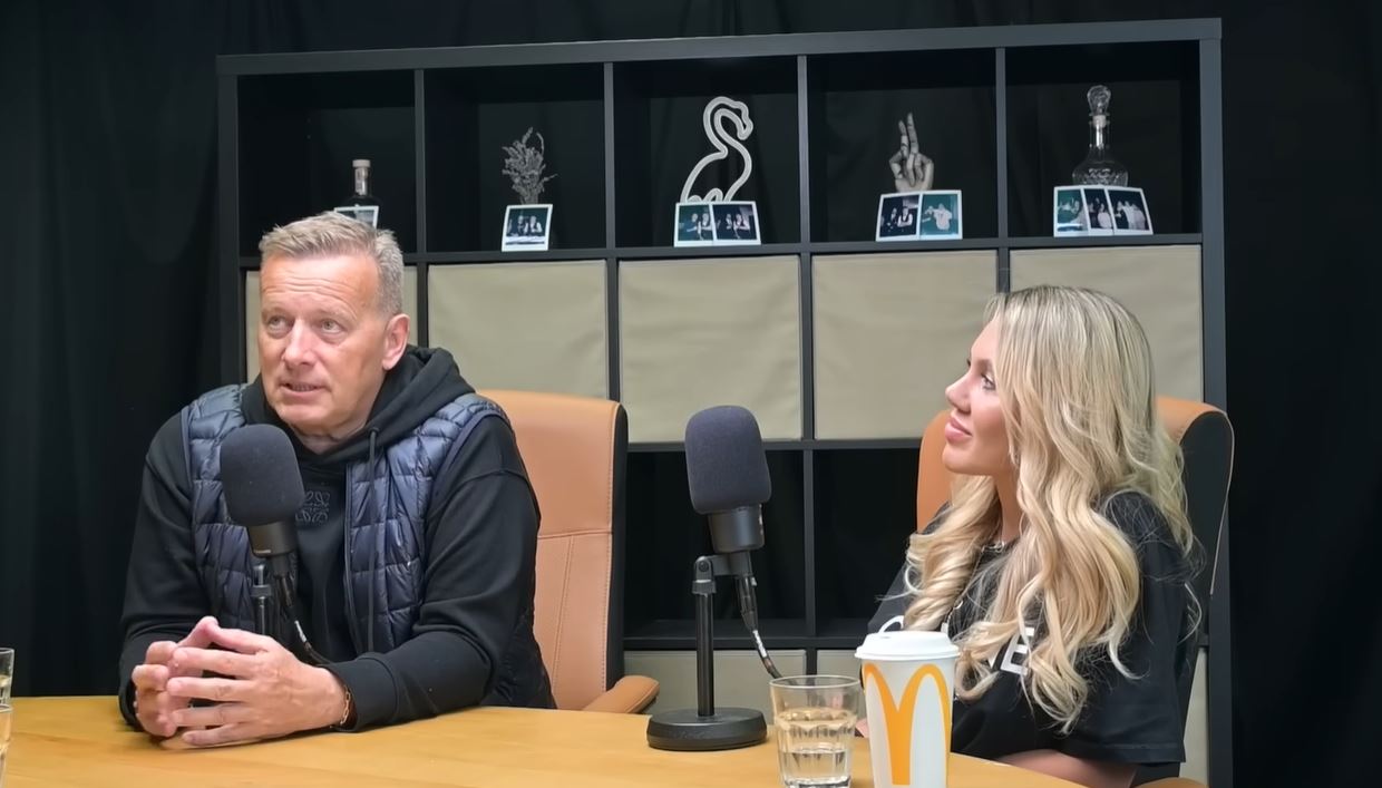 Dvojica počas rozhovoru v štúdiu so zavesenými polaroidmi a mikrofónmi na stole.