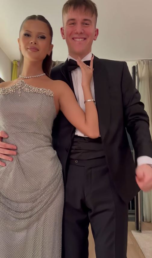 Pár vo formálnom oblečení s úsmevom, ona v šatách s perlami, on v obleku s motýlikom, pripravení na večernú udalosť.