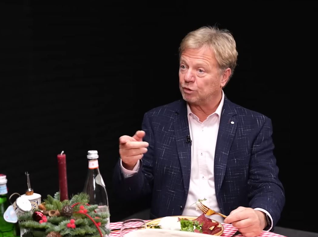 Muž v tmavom saku diskutuje pri jedle pri stole ozdobenom sviečkou a fľašou minerálky.