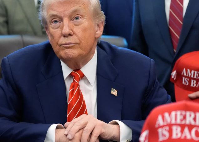 Loď som nepoznal.(Image description: Muž v modrom saku a červenej kravate s vlajkou USA na klopni medzi ľuďmi, ktorí majú