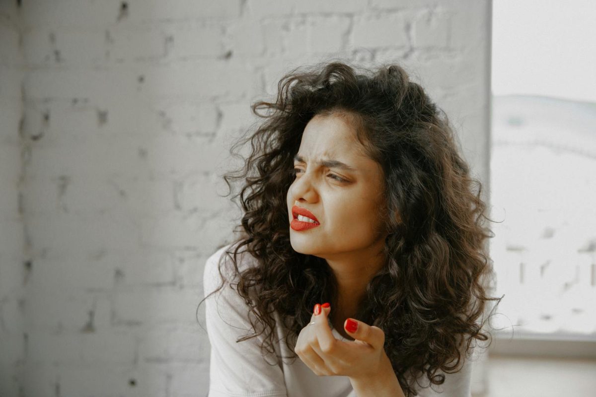 A brunette woman showing an expression of disgust against a brick wall.