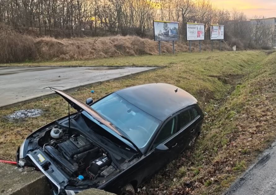 Auto v priekopách pri ceste, otvorená kapota, reklamné panely v pozadí, slnečný západ.