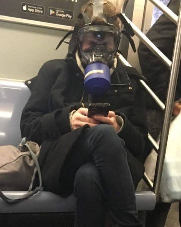 Osoba v plynovom maske sedí v metre a používa mobilný telefón.