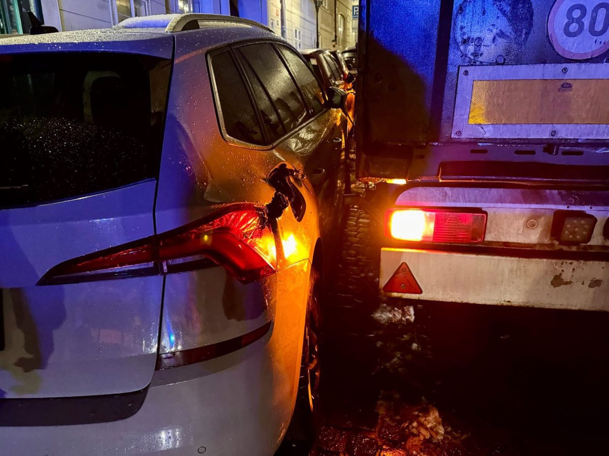 Parkovanie: Auto v úzkej uličke poškodené nákladným vozidlom, detailný pohľad na zadnú časť karosérie.