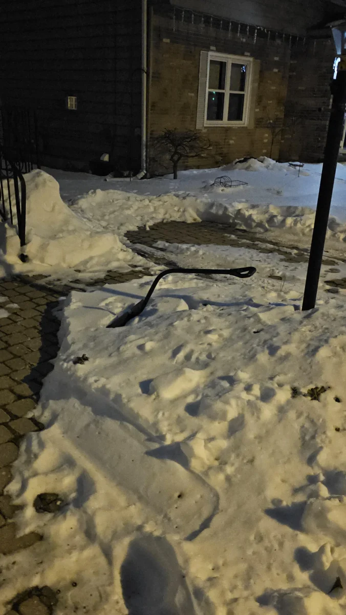 Domovská terasa zasypaná snehom, vedie k domu v zimnej noci pod pouličnou lampou.