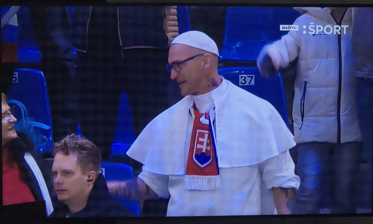 Fanúšik v bielom odeve so šálom Slovenska na športovom podujatí v hľadisku s ďalšími divákmi.
