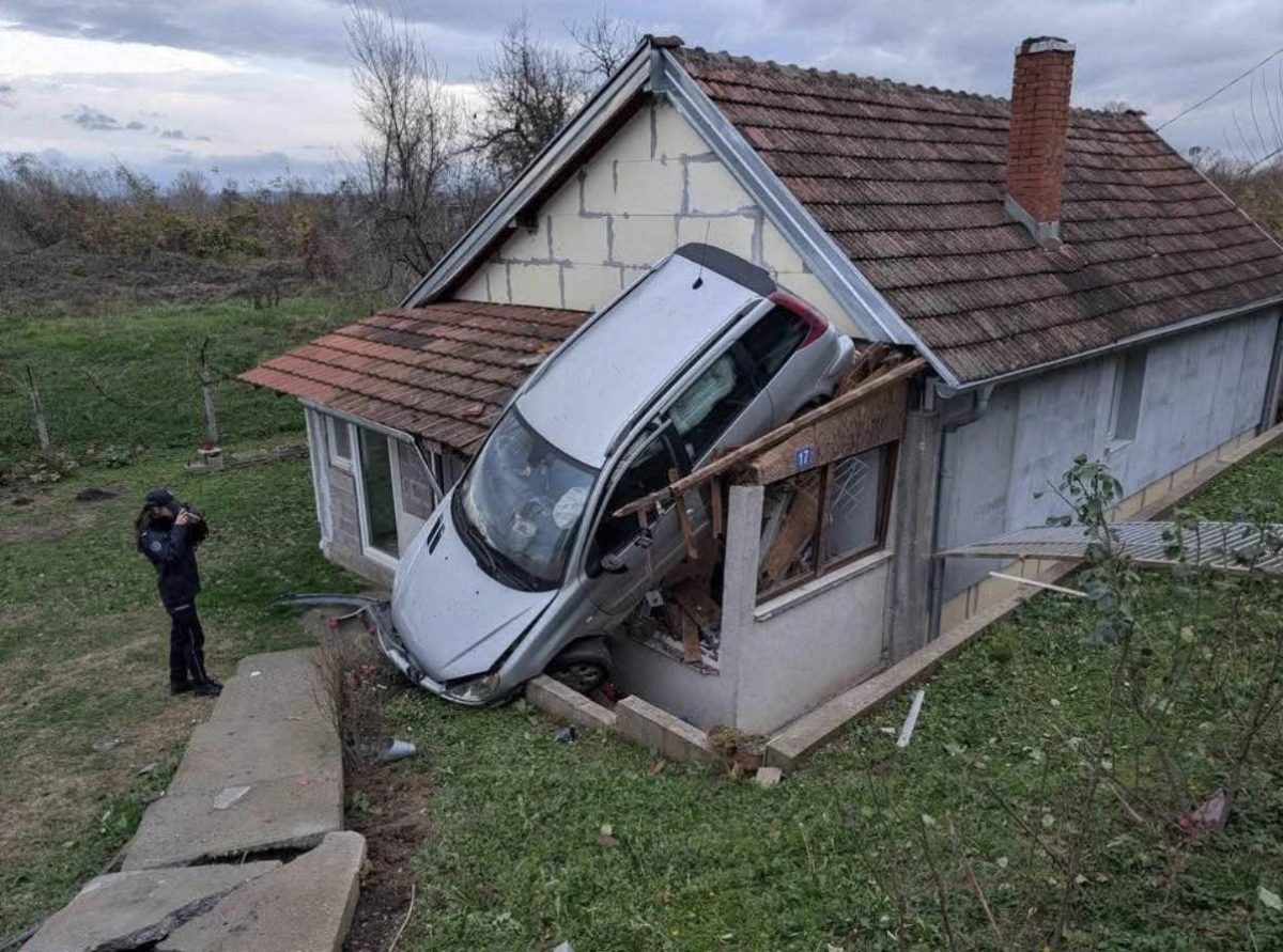 Auto narazené do domu, jeho predná časť trčí zo steny, polícia na mieste dokumentuje situáciu.