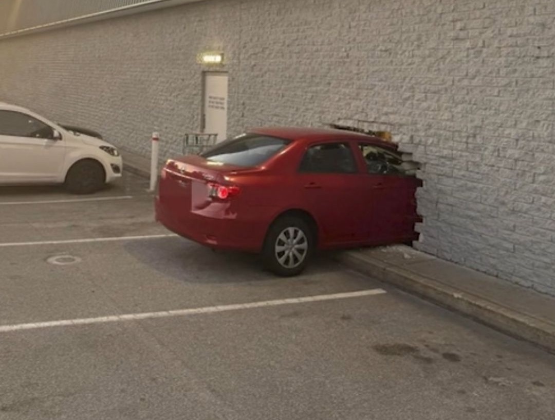 Červené auto nabúrané do tehlovej steny na parkovisku.