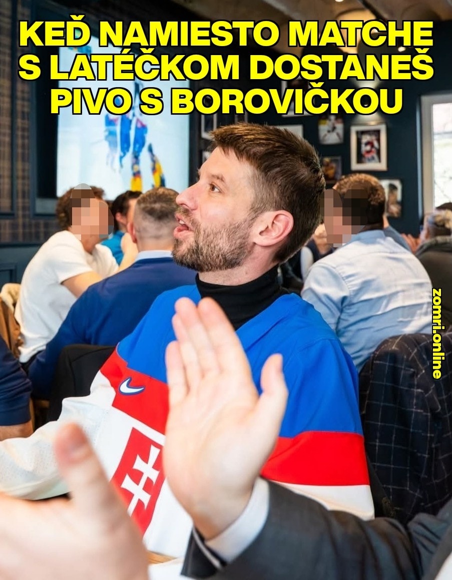 Muž v slovenskom drese s prekvapeným výrazom na skupinovom stretnutí ľudí v interiéri.