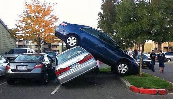 Modré auto zaparkované na striebornom aute na parkovisku, ľudia pozorujú situáciu.