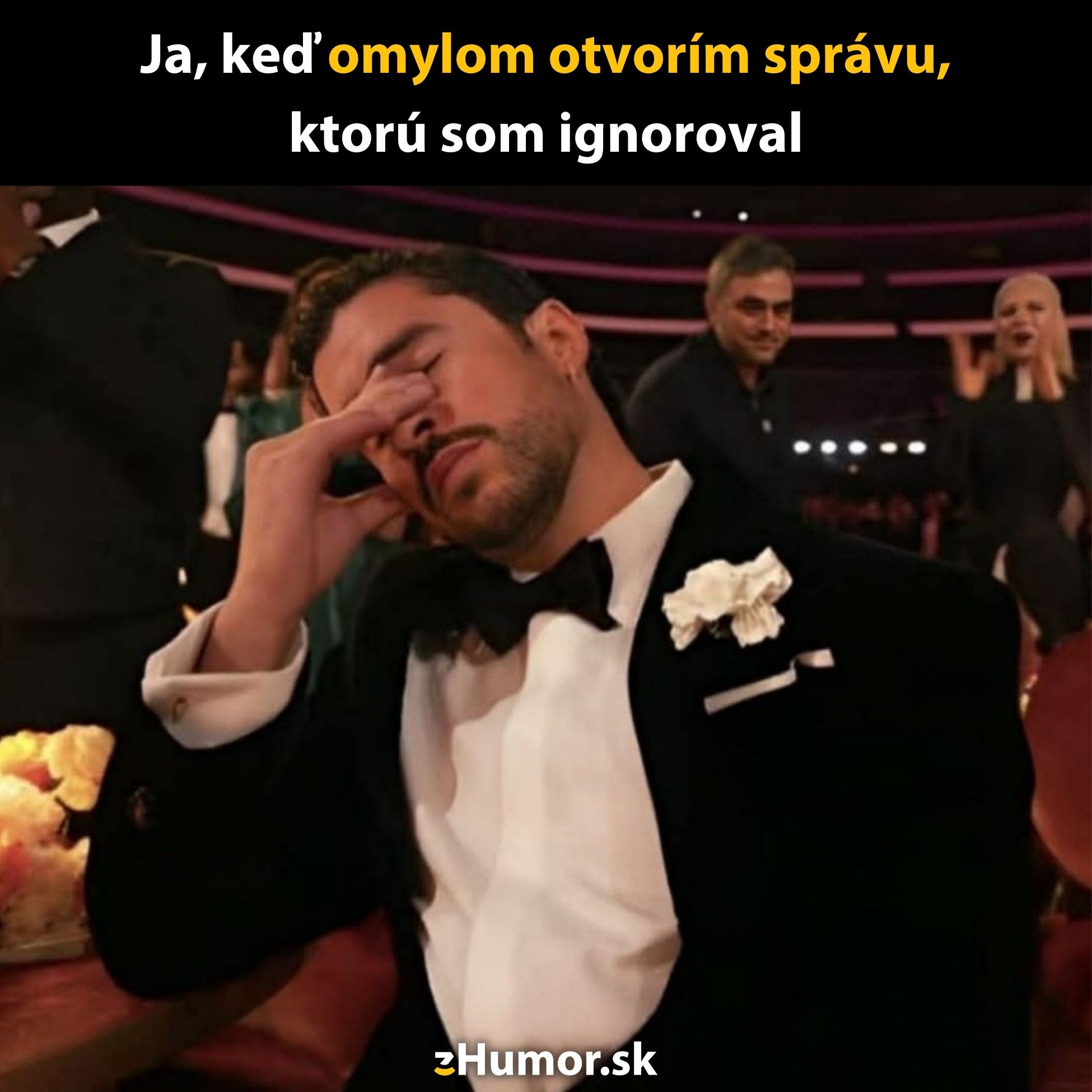Muž v smokingu drží ruku na tvári, vyzerá frustrovaný vo formálnom prostredí, ako keby sa unavene zamyslel.