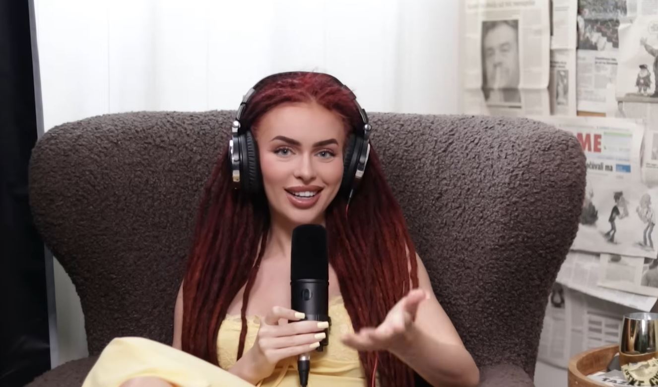 Žena s červenými vlasmi a slúchadlami nahráva podcast, sedí v kresle, držiac mikrofón.