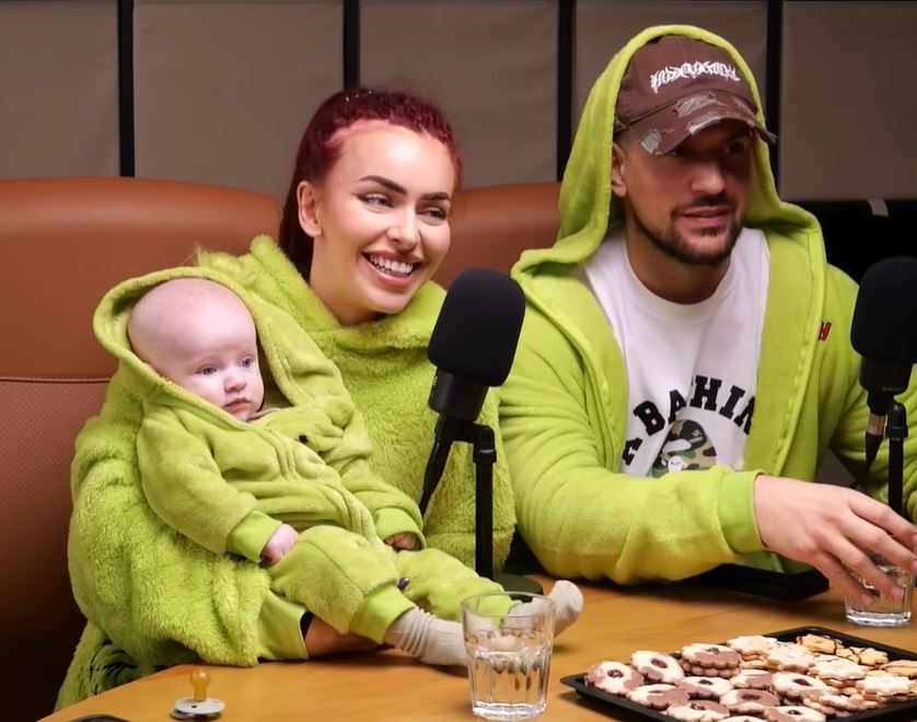 Rodina v zelených mikinách sedí pri stole s pohármi a sušienkami, pripravení na rozhovor s mikrofónmi.