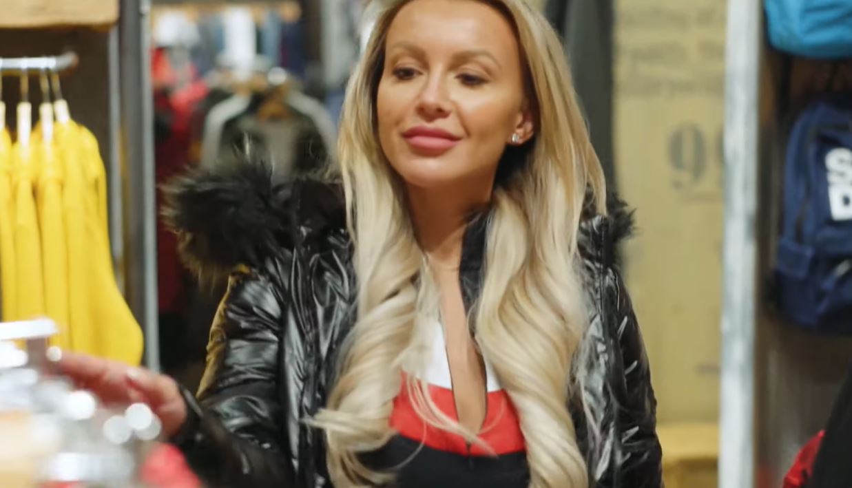 Žena v obchode skúmajúca ponuku oblečenia v zimnej bunde s kožušinovým golierom.