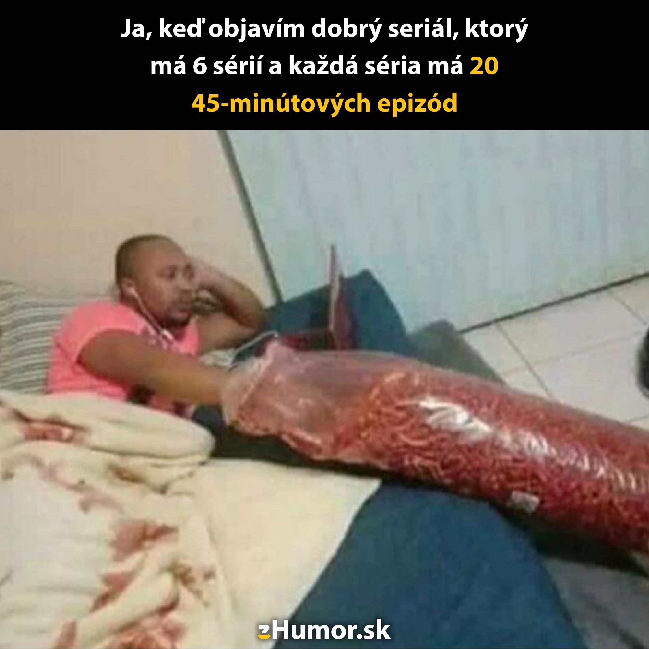 Muž sleduje seriál na notebooku, leží na gauči s veľkým vreckom chipsov.