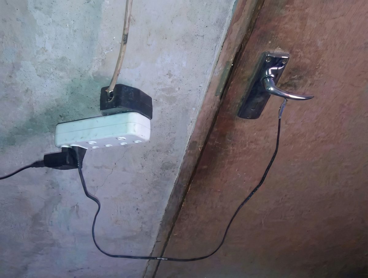Elektrická zásuvka a kábel zapojený na kľučku dverí pre improvizované zapojenie na stene miestnosti.