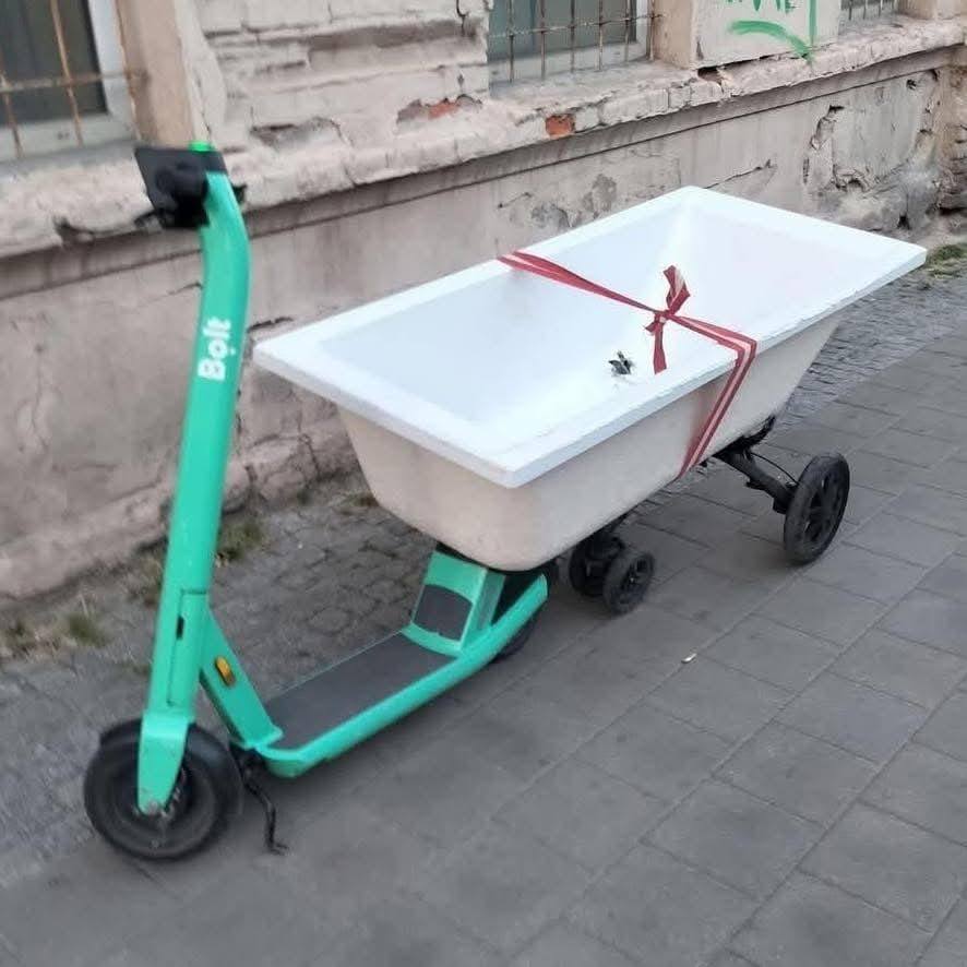 Elektrická kolobežka s pripevnenou vaňou na kolesách stojí pri stene na chodníku.