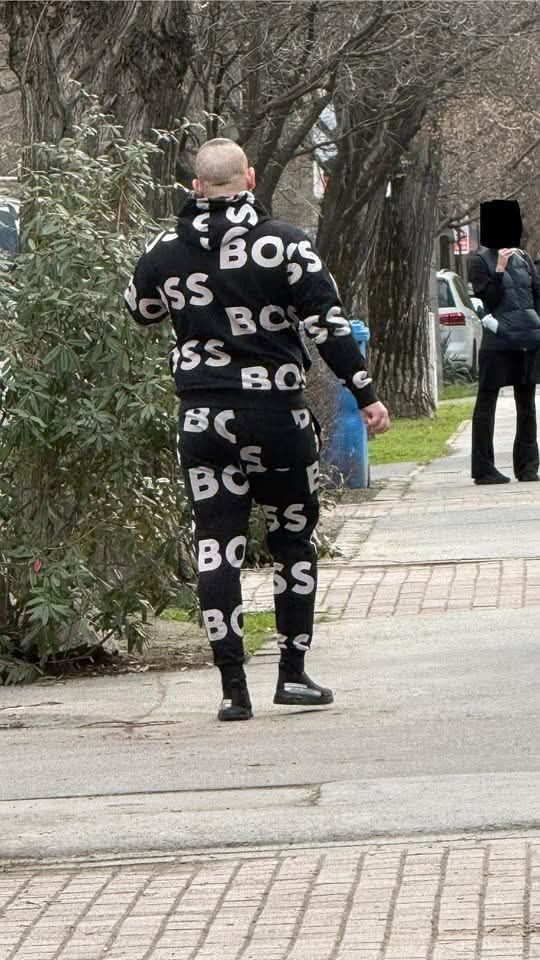 Muž kráča po chodníku v čiernej teplákovej súprave s nápisom BOSS.