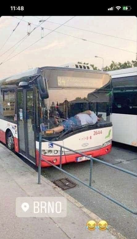 Muž ležiaci na čelnom skle autobusu v Brne, netradičná situácia na zastávke.