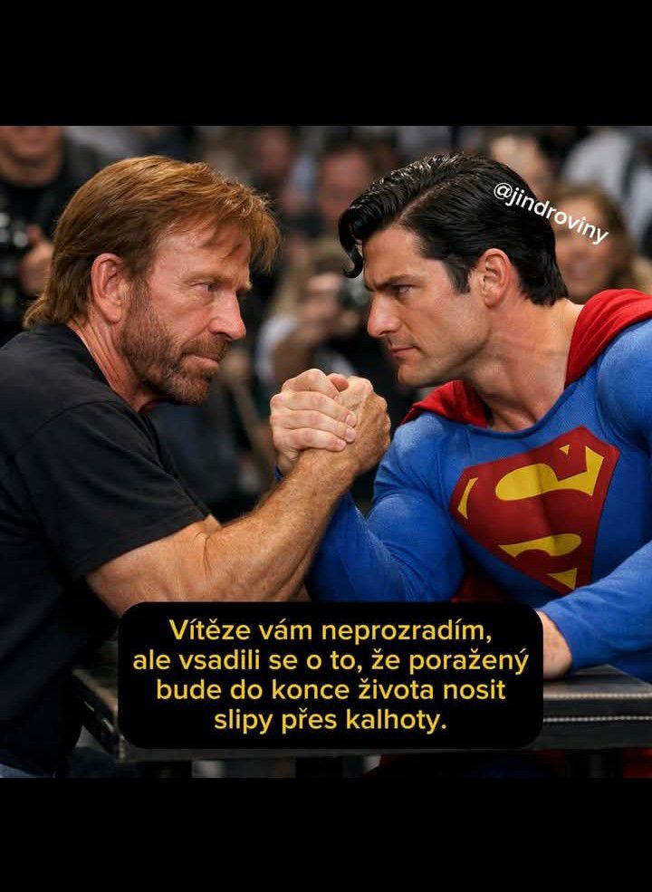 Dvaja muži, jeden v modrom obleku s červeným S, súperia v pretláčaní rúk pri stole, s publikom v pozadí.