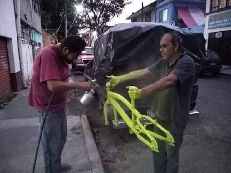 Dvaja muži striekajú žltú farbu na rám bicykla na ulici.