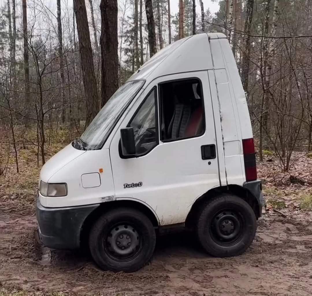 Malá biela dodávka s nezvyčajne vysokou strechou stojí na lesnej ceste.