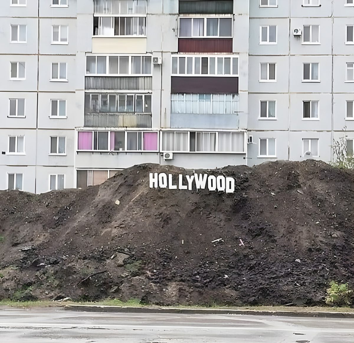 Viacposchodový panelák s nápisom Hollywood na hromade zeminy v popredí.