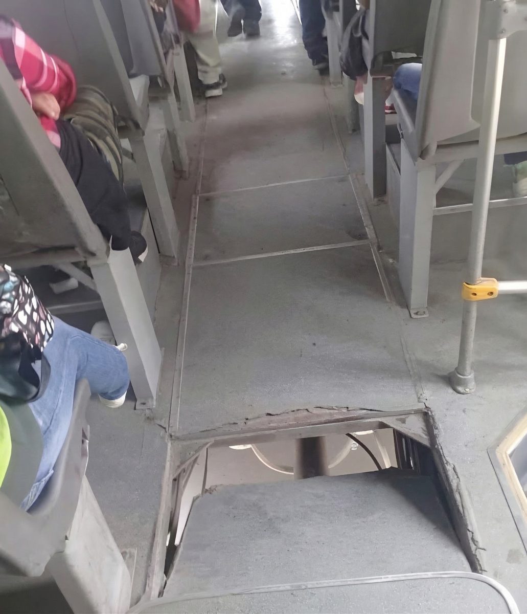 Podlaha autobusu s otvorom medzi sedadlami, ukazujúca opotrebovanie a potenciálne nebezpečenstvo pre cestujúcich.