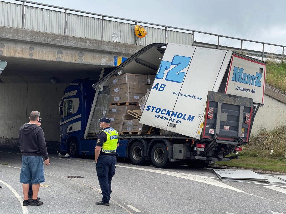 Nákladné auto zaseknuté pod mostom s policajtom a civilistom na mieste incidentu.