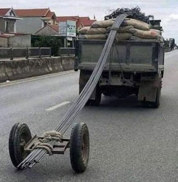 Nákladné auto prevážajúce kovové tyče s provizórnym podvozkom na ceste.