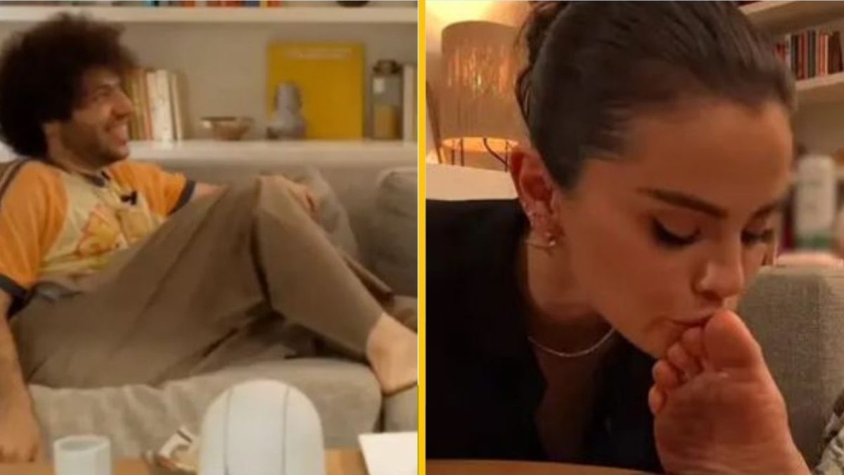 Osoba relaxuje na gauči; žena vedľa dáva pusu na nohu. Útulný moment v obývačke.