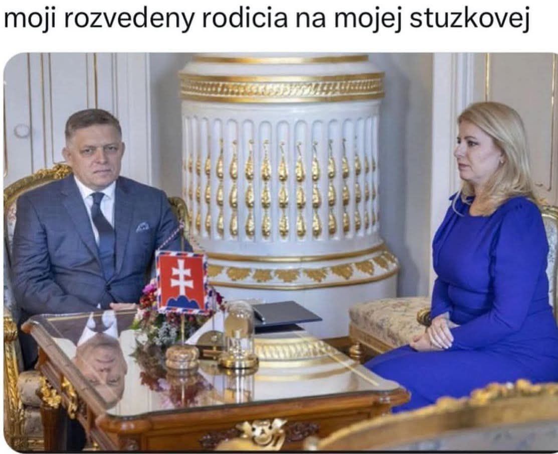 Dvaja ľudia v elegantnom prostredí sediaci oproti sebe za zdobeným stolom so slovenskou vlajkou.